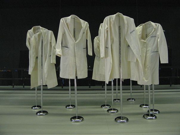 identical white coats are hung over metal posts